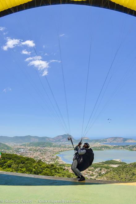 Imagem de um rapaz posicionando paraquedas para salto e ao fundo a linda vista de Niteroi.